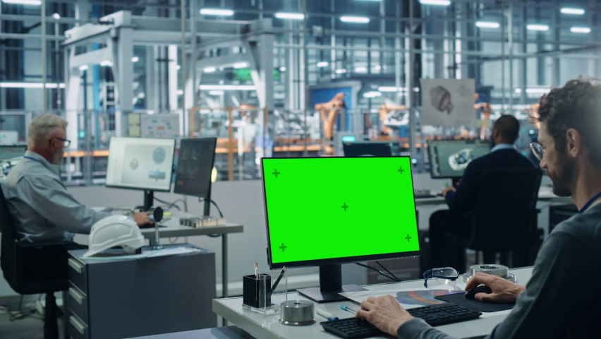 Car Factory Office: Caucasian Male Automotive Engineer Sitting at His Desk Working on Green Screen Chroma Key Computer. Automated Robot Arm Assembly Line Manufacturing. Over Shoulder Medium Shot | Shutterstock HD Video #1077501932
