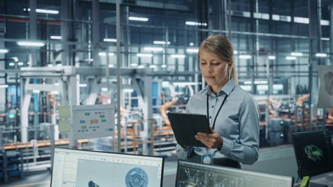 Car Factory Office Concept: Portrait of Successful Female Chief Automotive Engineer Using Tablet Computer to Design and Optimize Automated Robot Arm Assembly Line Manufacturing Electric Vehicles