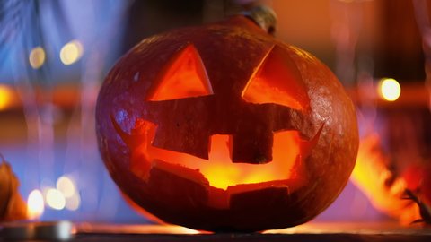 Carved Halloween pumpkin head illuminated from inside, bokeh lights on background. Jack o lantern, Halloween home decor.