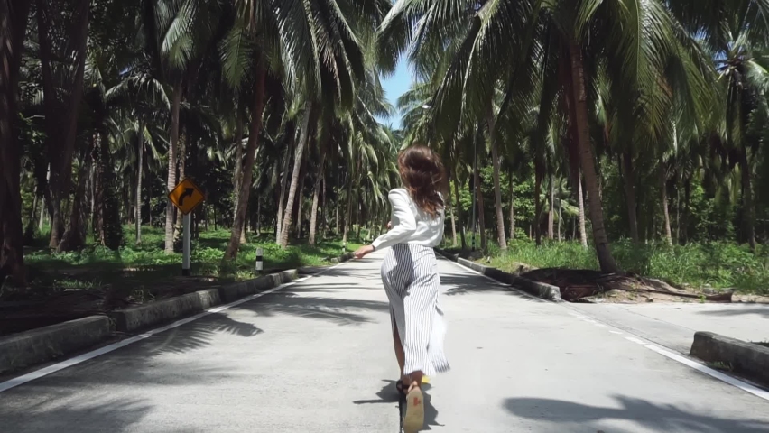 Rear view: a young girl of European appearance is running along the road, there are many palms around