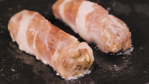 Preparation of meat dish from minced meat wrapped in bacon with white veins. The chevapchichi are fried in a hot pan in oil. Beautiful wallpaper of cooking for restaurant. Slow motion. Close up.