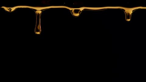 Golden drops of honey drip on a black studio background. The sweet thick liquid drips down. Transparent colorful syrup or oil droplets flowing down. Close up. Slow motion.