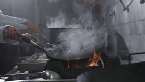 Chefs cooking wok noodles in a skillet with blazing fire. Closeup of a chef throws ingredients into a frying pan while preparing Chinese food. Slow motion 4K video