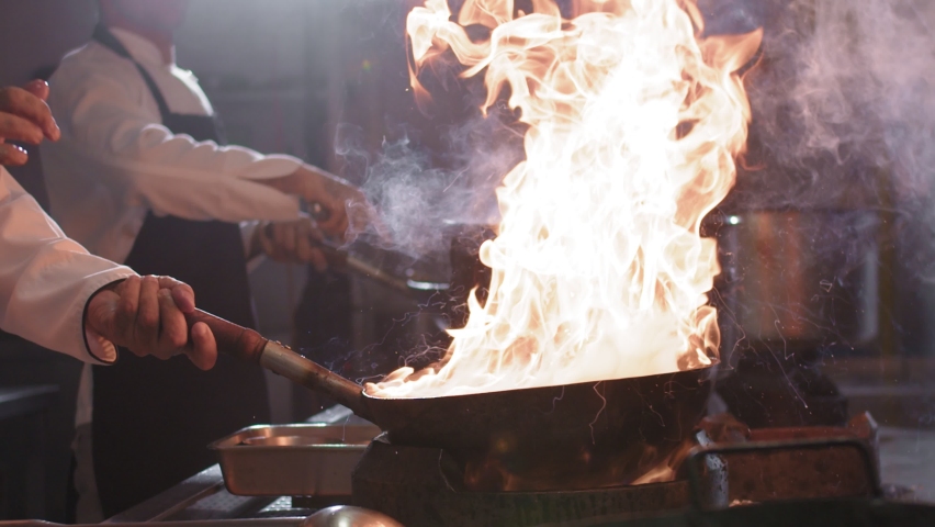 Chefs cooking wok noodles in a skillet with blazing fire. Closeup of a chef throws ingredients into a frying pan while preparing Chinese food. Slow motion 4K video Royalty-Free Stock Footage #1077507593