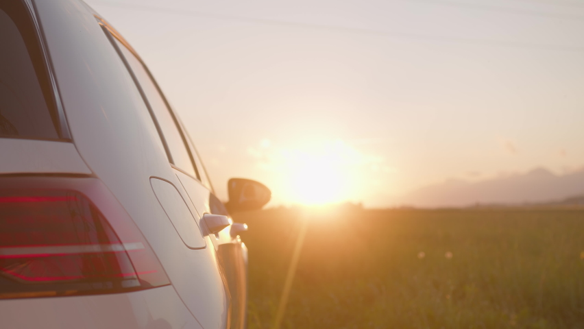 Handheld shot of a Caucasian woman charging an electric car at a charging station near a highway at sunset, using her smartphone while waiting Royalty-Free Stock Footage #1077510053