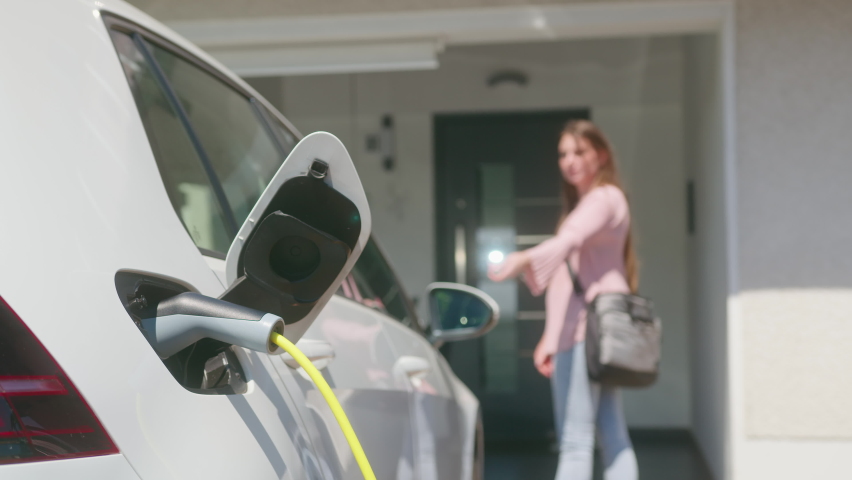 Close up of a electric car charger with Caucasian female silhouette in the background, locking a car and entering the home door Royalty-Free Stock Footage #1077510128