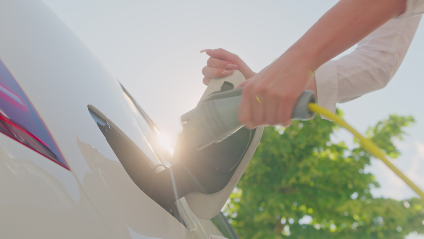 Close up shot of a Caucasian female hands opening an electric car charging socket cap and plugging in a charger Royalty-Free Stock Footage #1077510173