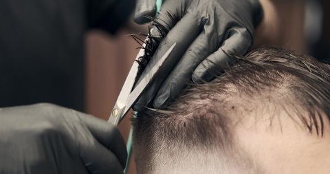 Barber hands cutting hair of man with comb and scissors