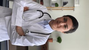 Vertical video for sharing social network services 30s smiling Indian woman therapist in white uniform smile look at camera at workday in hospital office, ready for patient visit, medical care concept