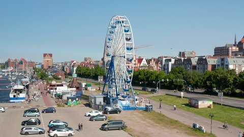 Rising view of running Ferris wheel. People enjoying time on attraction. Ascending and tilting down footage with city in background. Rostock, Germany in 2021