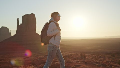 Happy smiling woman with backpack in red southwest American desert at sunset or sunrise, enjoying freedom of travel and lifetime memories, youth and happiness. Watching sunset with beautiful landscape