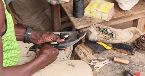 NIMA, GHANA - 20 JUL 2021: Old Man Shoe maker outdoors cobbler shop fix Accra Ghana. Old Muslim shoe maker and cobbler. Poverty section of Accra Ghana. Happy to repair people shoes for very little inc