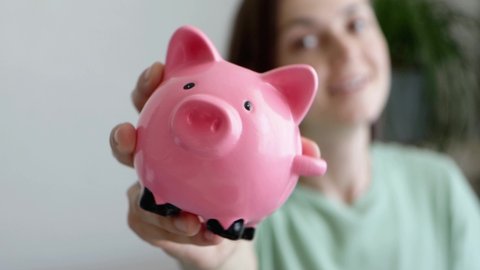 Portrait of happy young woman is smiling and shaking pink piggy bank. Savings and investment concept