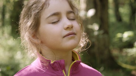 Portrait Child Girl Exhaling Fresh Air, Taking Deep Breath, Reducing Stress in Forest. Dreamy Peaceful Relaxed Smiling Kid Girl Breathing Fresh Air Nature, Tranquil Caucasian Child Alone Outdoors.