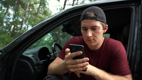 man smokes vape and uses the phone while sitting in the car.