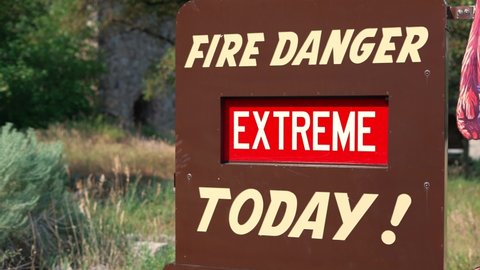 EXTREME Fire Danger Today red and white sign on brown metal board wide shot that whips straight up to view mountains at national park during wildfire crisis in the US and world. In 4k 60fps real time.