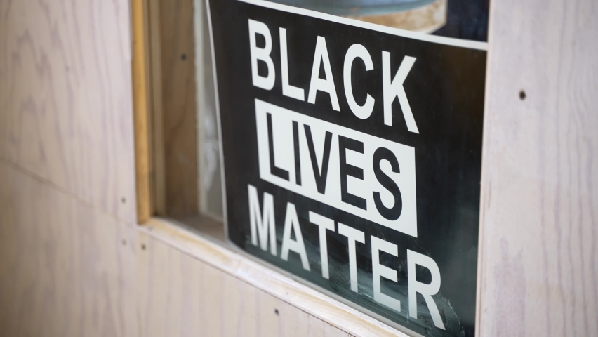 Black Lives Matter sign in small local business owner’s window with camera slowly panning left revealing yellow couch in glass reflection. In 4k 30fps slowed from 60fps. Royalty-Free Stock Footage #1077534314