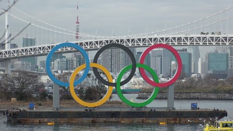 TOKYO, JAPAN - FEB 2020 : The five ring symbol of the Olympic Games in front of Odaiba Rainbow Bridge. Shot in day time. 2020 summer Olympic postponed until 2021 due to coronavirus (COVID-19).