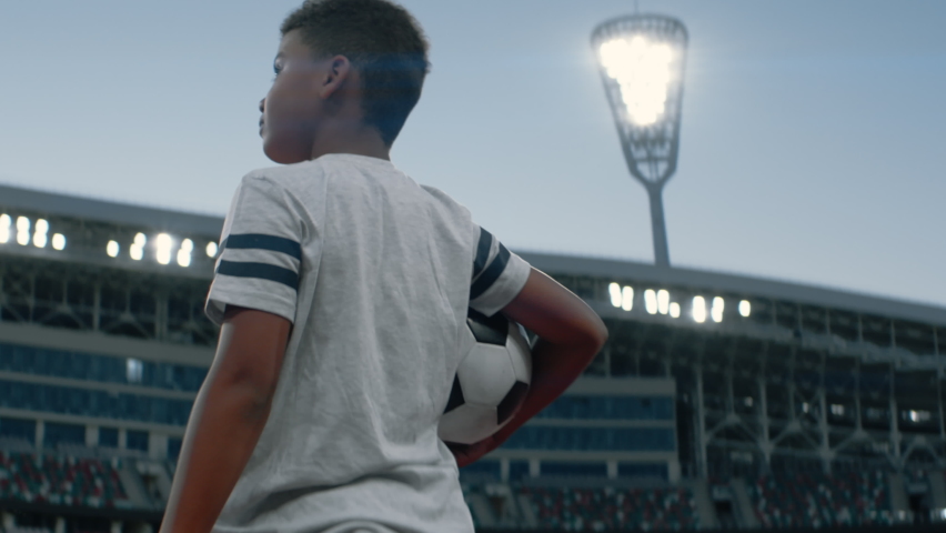 Portrait of African American Black dreamer kid boy walking onto the field of huge soccer football stadium, holding a ball, dreaming of becoming professional player, soccer star | Shutterstock HD Video #1077536018
