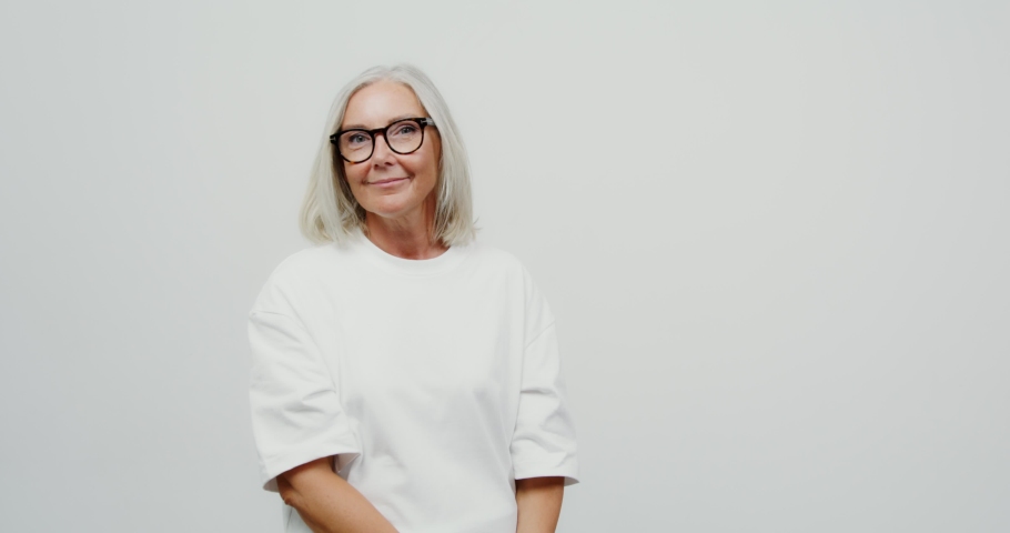 Adult gray-haired woman playing with multi-colored paper bags in her hands, happy after shopping. Shooting against a solid blue background.
