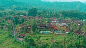 Aerial top view on traditional balinese architecture with traveler man enjoying summer vacation at swimming pool on Villa in Ubud. 4K Aerial UHD video clip.