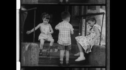 1960s New York City, Brother and Sisters playing out front of a bodega storefront. Two Young boys ride a  wagon, go-cart, or pedal car below a truck. 4K Overscan of Vintage Archival 16mm Film Print