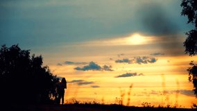 Silhouette of a woman with a baby in her arms, walking in the distance against the backdrop of a sunset in a field.
