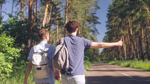 Male backpackers making thumb gesture to hitch ride, friends traveling together