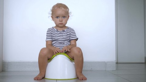 Caucasian toddler on a potty against white wall looking straight to the camera. Potty training concept