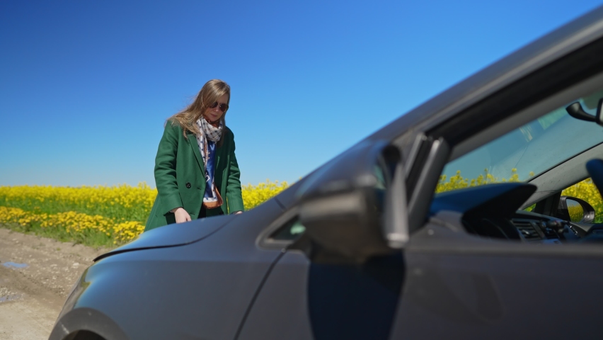 Woman in the coat opens the hood of the car.