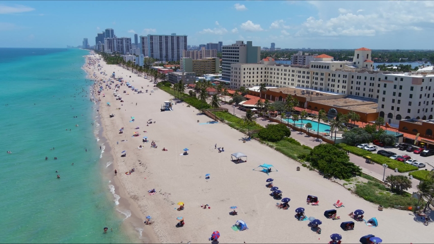 Aerial Flying Hollywood beach Ocean coastline south over water sunny beach with condos and boardwalk swimmers