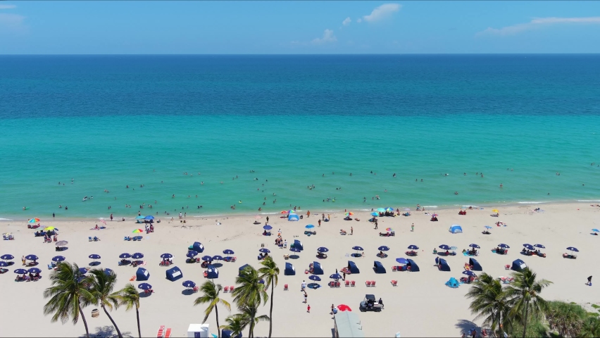 Aerial Hollywood Florida fly south along beach coastline and ocean view on sunny days with umbrellas