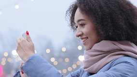 Side view young attractive afro american woman with curly hair in warm outerwear standing at city park in winter time, looking at her phone online dating chatting in app social network smiling laughs - Powered by Shutterstock - Get 15% off with code: PIKWIZARD15