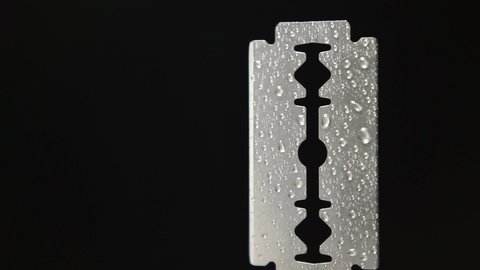 Traditional razor blade with water droplets on black background. Macro shooting. Rotation