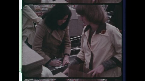 1970s Buffalo, NY, Grocery Store Clerk bags groceries in brown paper bag as Woman writes check from a checkbook for groceries purchased at  Supermarket. 4K Overscan of Vintage Archival 16mm Film Print