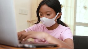 Asian girl in medical face mask watching video online content from computer laptop at home, Home quanrantine and new normal lifestyle concept
