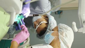 Modern dental clinic. Vertical video: Medical team working with sterilized tools wearing face shield, mask, and gloves during treatment in a new stomatological clinic. Dentist treating kid's teeth. 