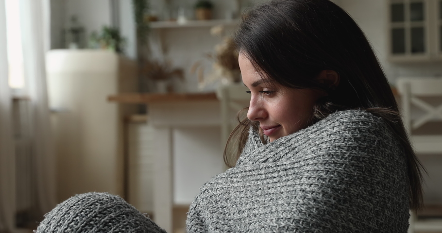 Covered in warm knitted plaid stressed unhappy young woman shivering, suffering from low temperature inside, feeling unhealthy. Confused millennial homeowner having problems with central heating. | Shutterstock HD Video #1077576725