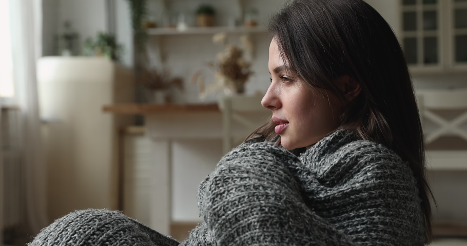 Covered in warm knitted plaid stressed unhappy young woman shivering, suffering from low temperature inside, feeling unhealthy. Confused millennial homeowner having problems with central heating. Royalty-Free Stock Footage #1077576725