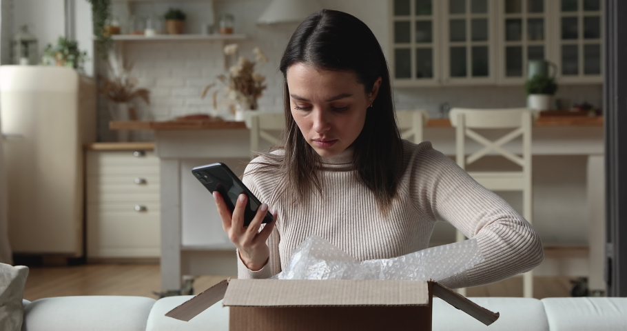 Unhappy young woman unboxing parcel, checking internet order in mobile shopping app, dissatisfied with received wrong crashed item, stressed client having negative experience, purchasing goods online. Royalty-Free Stock Footage #1077576767