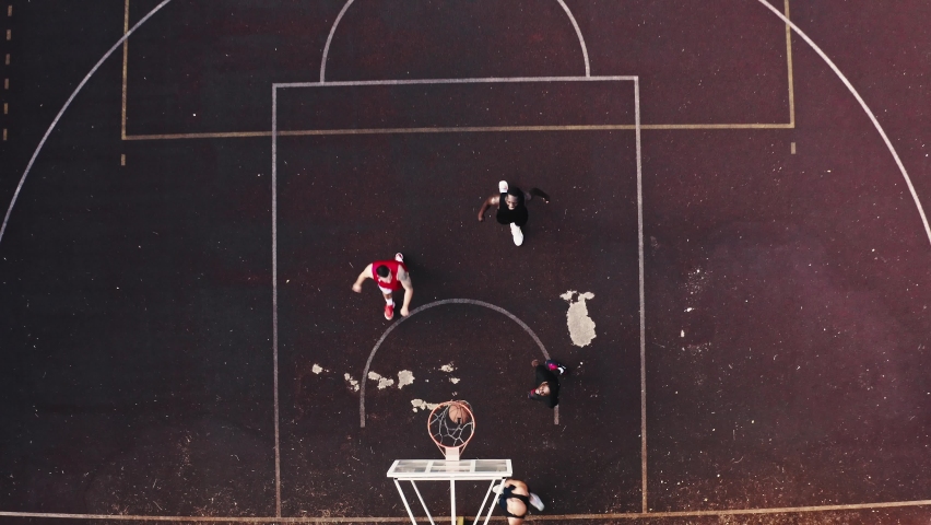 Sports life in the city. Aero footage view of a basketball court with professional basketball players of different races. Approaching, moving from top to bottom to the basketball hoop and finish.