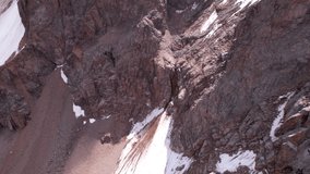 High rocky mountains are sometimes covered with ice and snow. A huge glacier passes between the peaks. The ice is gradually melting. The stones are lying on glacier. Steep cliffs. The view from drone