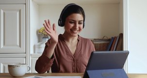 Happy young Indian woman in headphones start videoconference on digital tablet by business or study sit in homeoffice room. Video call event, apps, on-line tutor start virtual meeting class concept