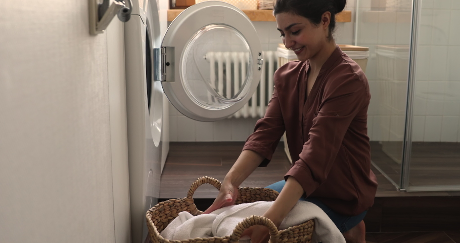 Indian housewife puts bath towels into washing machine do housework in laundry room. Housekeeper busy in regular routine house work. Modern washer-dryer appliance detergent ad, cleaning chores concept | Shutterstock HD Video #1077583937