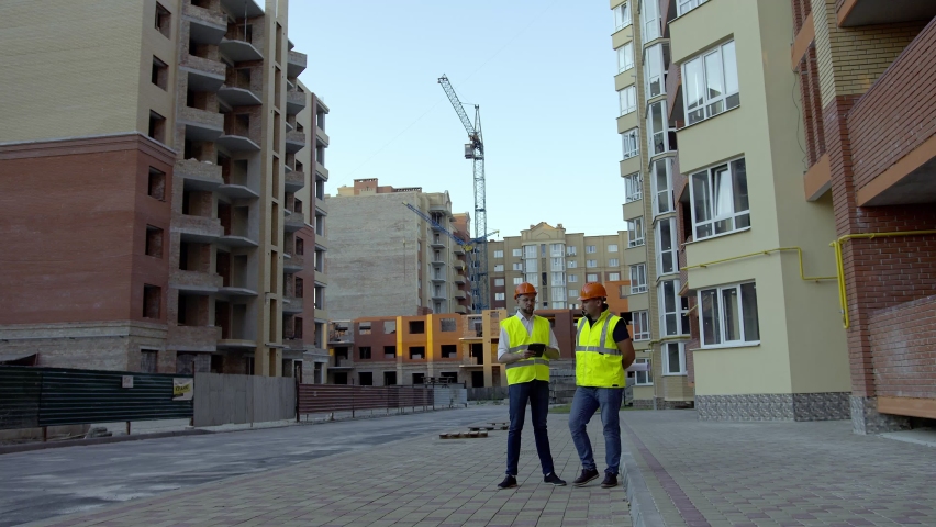 Two young builders stand and speak with each other, big building