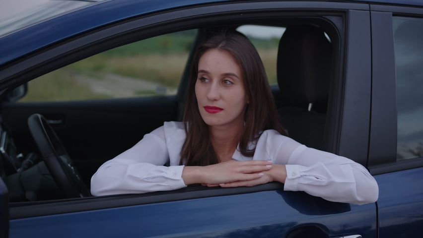 Nice young girl looks on the camera and smiles, white shirt, blue electric car