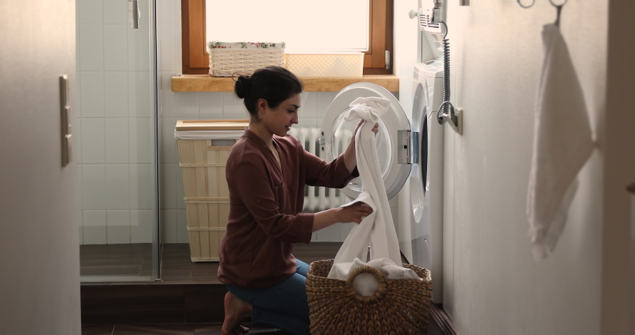 Indian housewife young woman do housework, busy in regular housekeeping work put bath towels into washing machine, turns on modern washer-dryer appliance in cozy laundry room. Household chores concept Royalty-Free Stock Footage #1077590324