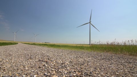 Low slider motion across a gravel road of windmills turning near Pincher Creek Alberta Canada.