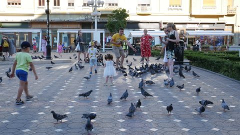 Timisoara, Romania - 07.15.2021: People an tourist in the center of Timisoara taking pictures and playing with pigeons in Victory Square