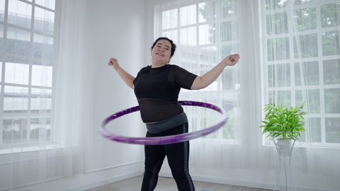 Fat Asian woman playing hula hoop to lose weight cheerfully in her room. health and weight loss concept